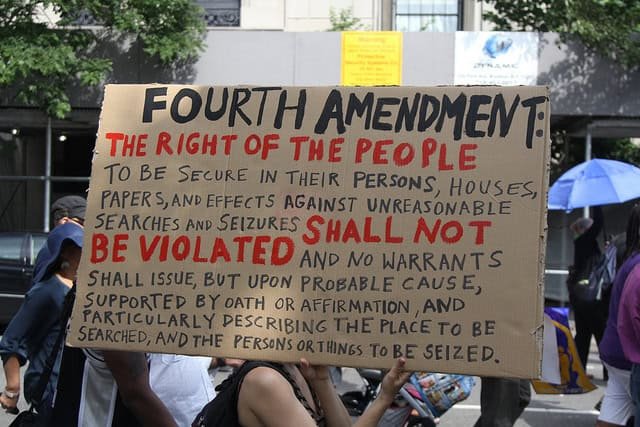 Article about policies on performing a strip search. Here a protestor holding a sign that reads the significance of the Fourth Amendment rights.